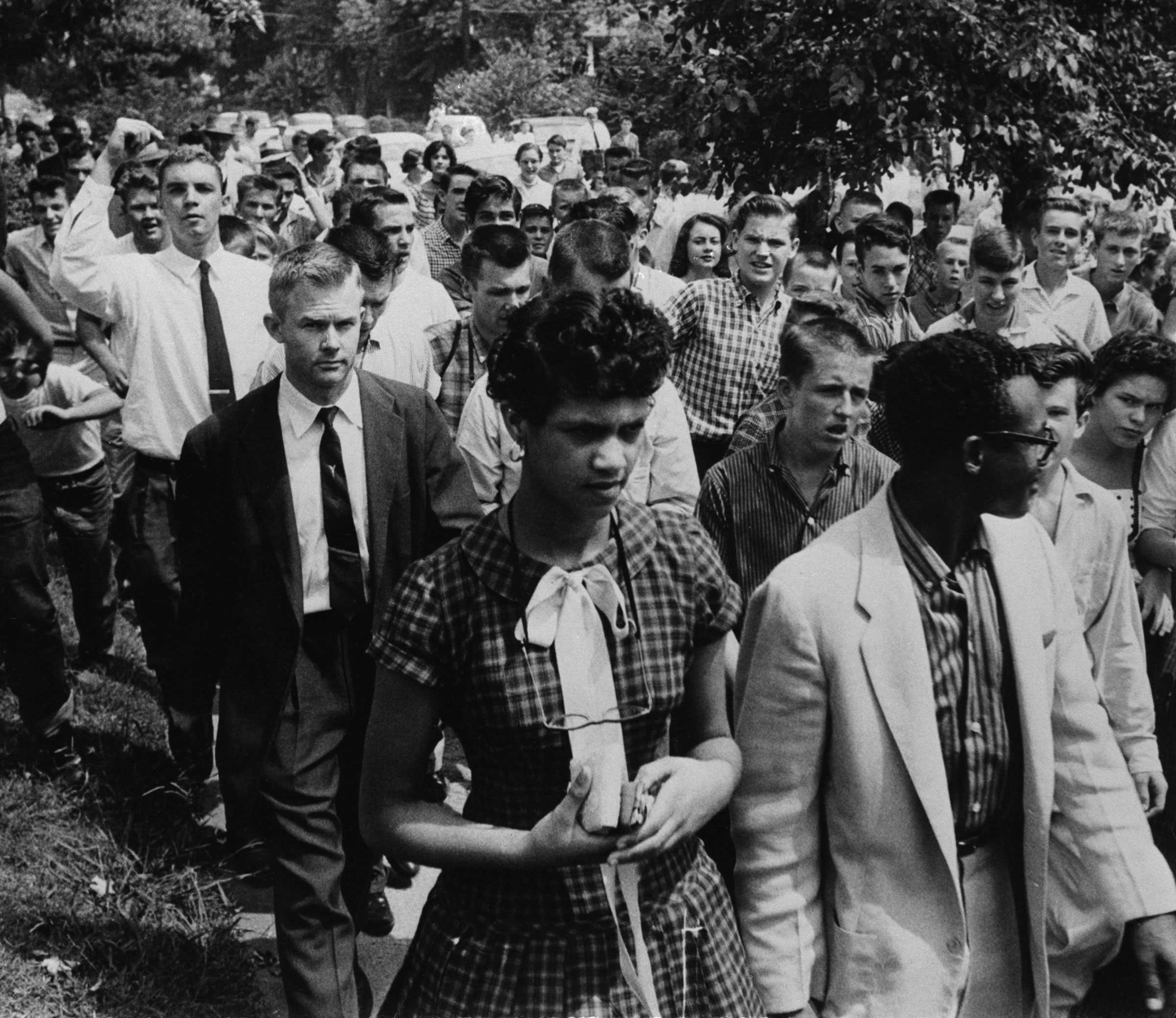 Dorothy Geraldine Counts walks besides her father to enroll in school as large crowd of white people follow.