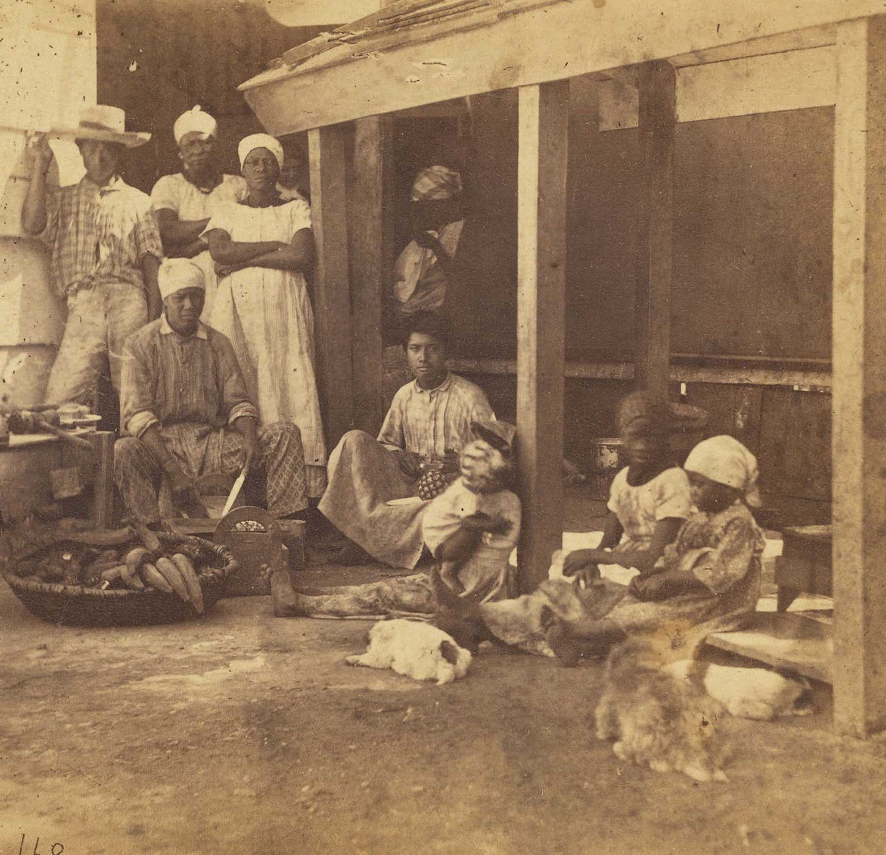 A dipict of a family outside a building. Animals and children sit on the dirt. Adults stand behind a large basket of food.