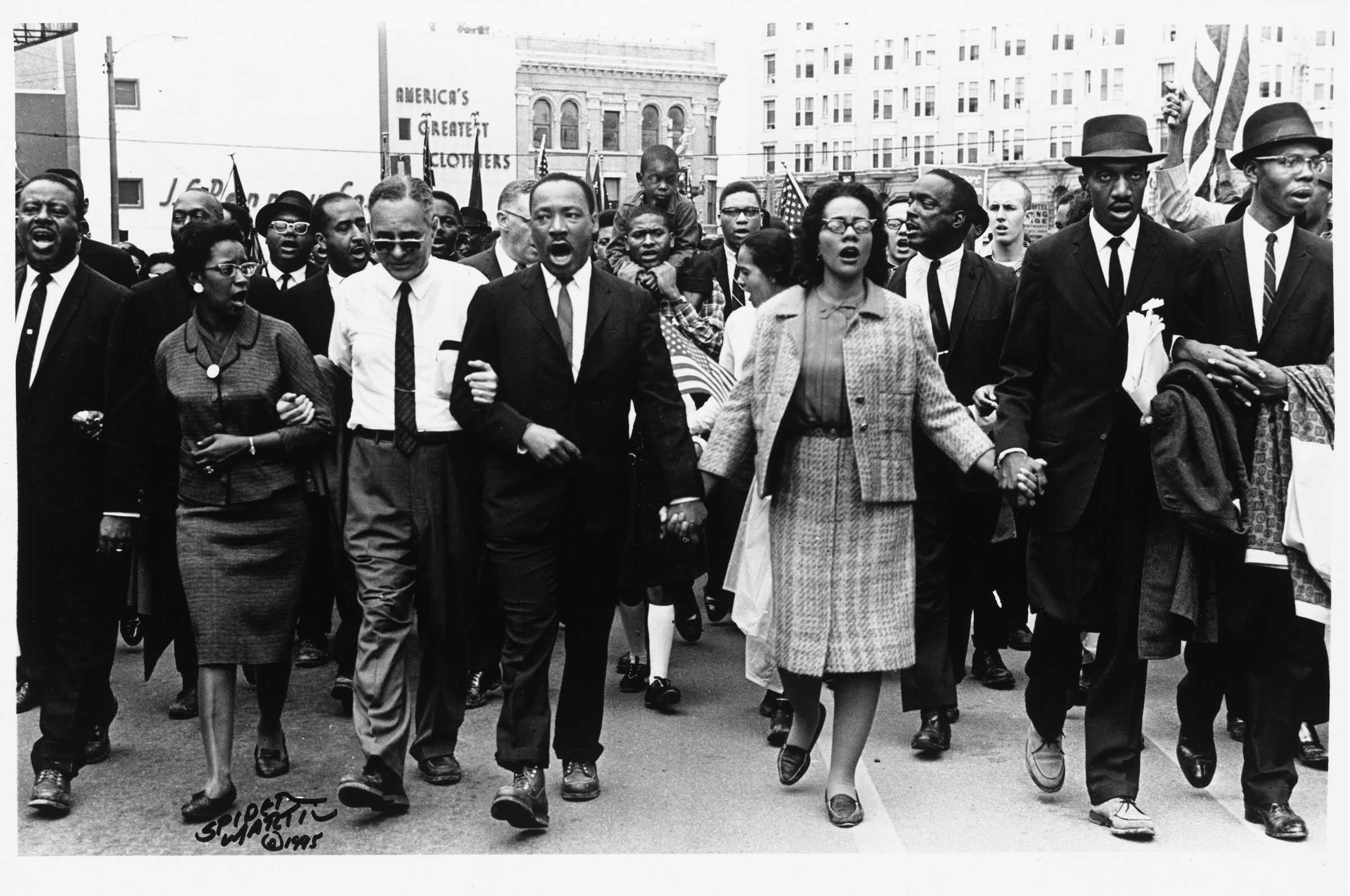 A black-and-white photograph of Martin Luther King, Jr. leading marchers into Montgomery, Alabama, during the "Selma to Montgomery" march.